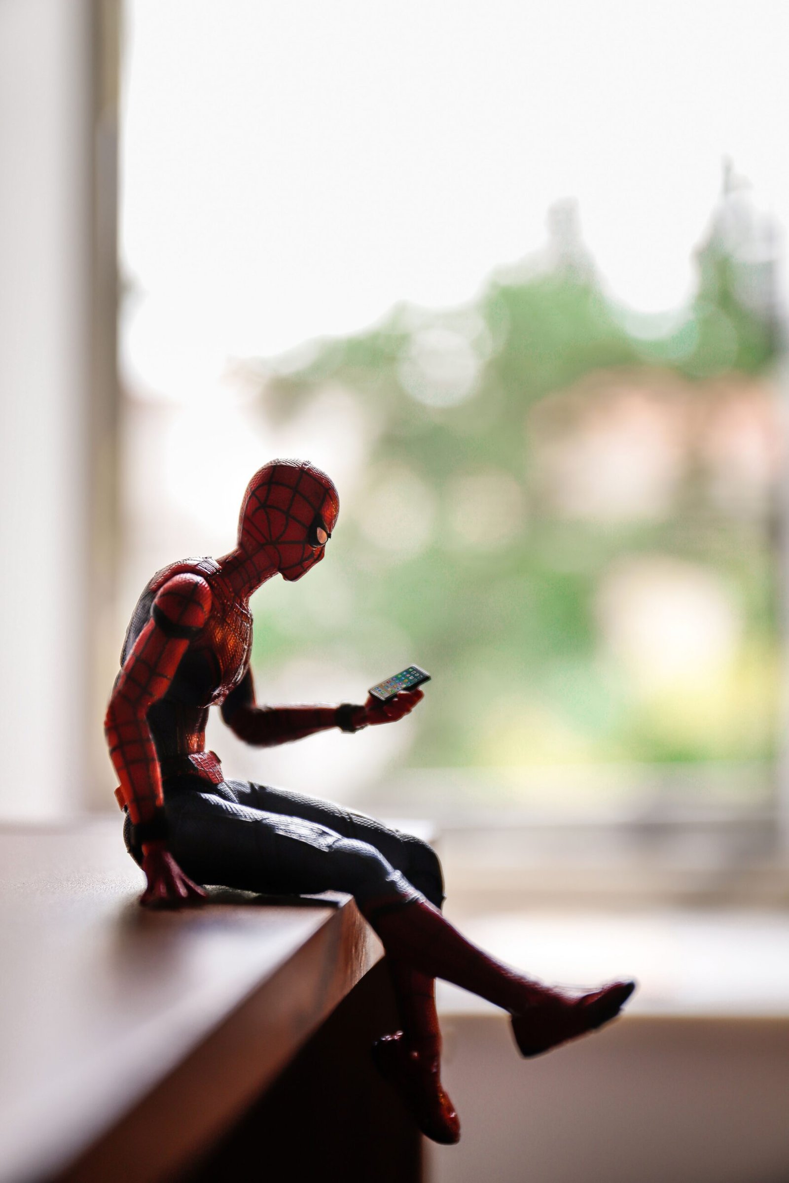 Spider-Man action figure sitting on a table and holding a smartphone